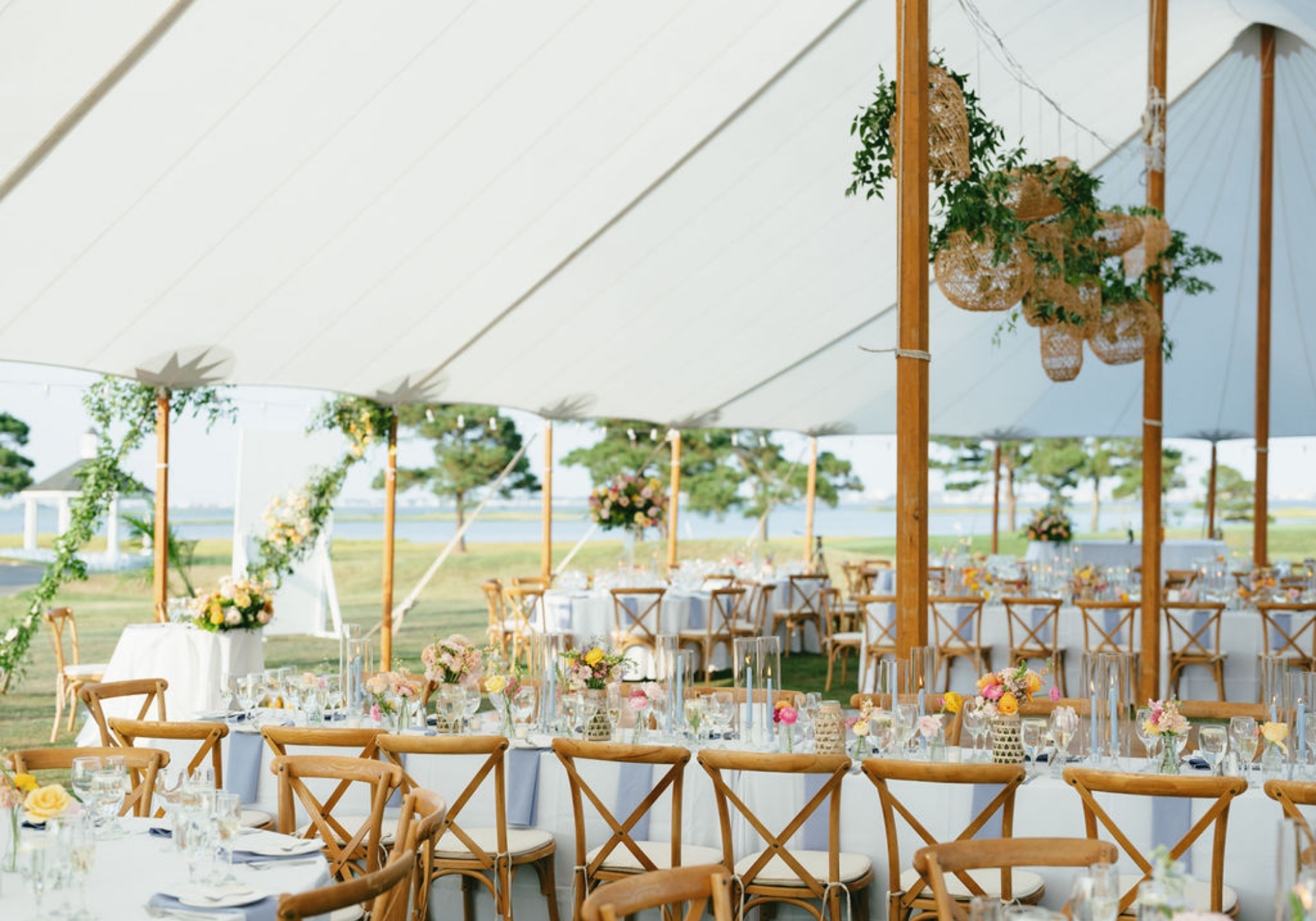 Sailcloth tent reception overlooking the bay with long farmhouse tables, wooden cross-back chairs, woven lanterns, and garden-inspired florals on Maryland's Eastern Shore.