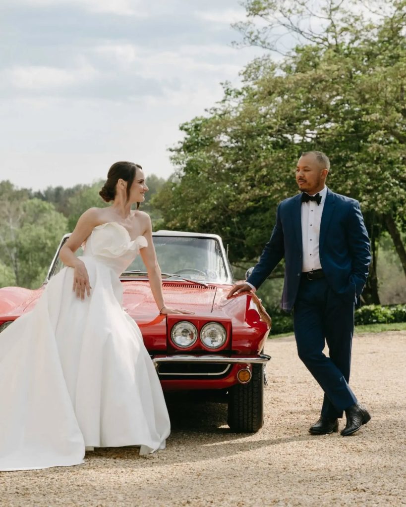 bride and groom looking at each other with leaning on vintage car