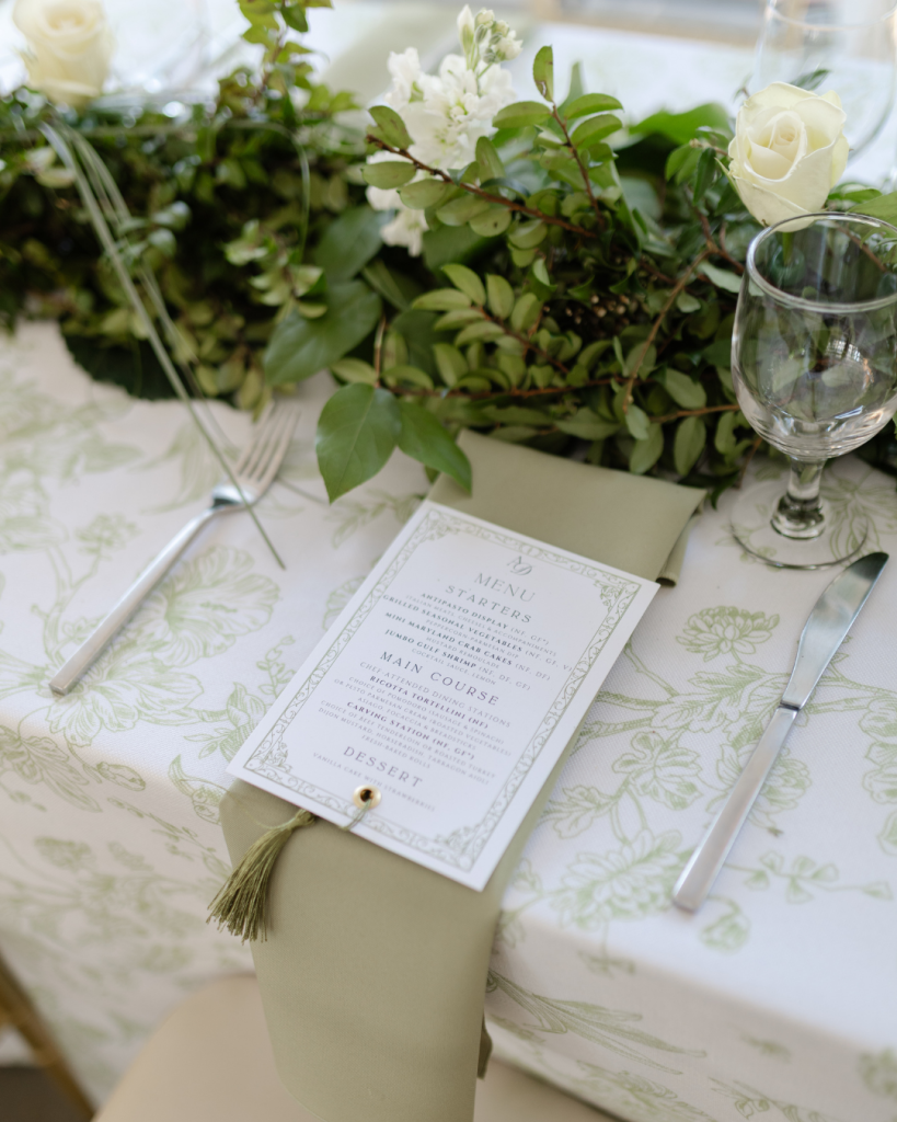 Elegant outdoor reception table with green patterned linens, floral centerpiece, and printed menu at The VanLandingham Estate wedding in Charlotte.