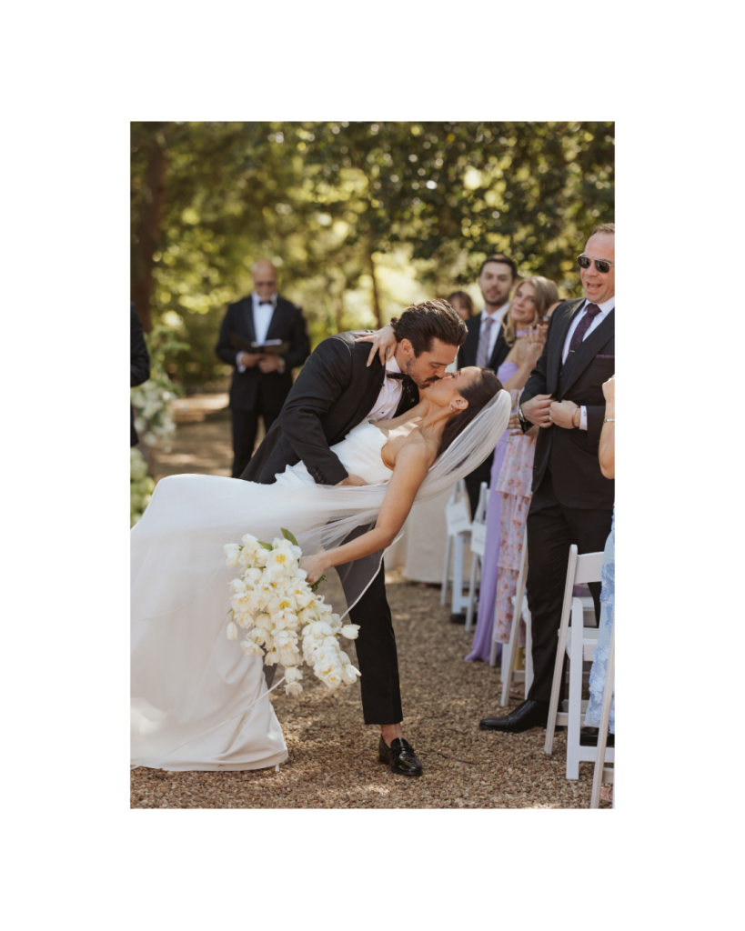 Bride and groom share their first kiss after the ceremony surrounded by cheering guests during their outdoor wedding in Charlotte.