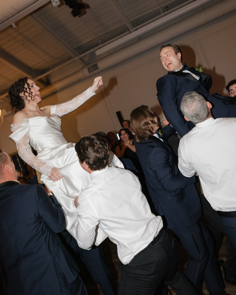 Bride and groom celebrate during the Horah as guests lift them into the air during their wedding reception at The Casey in Charlotte.
