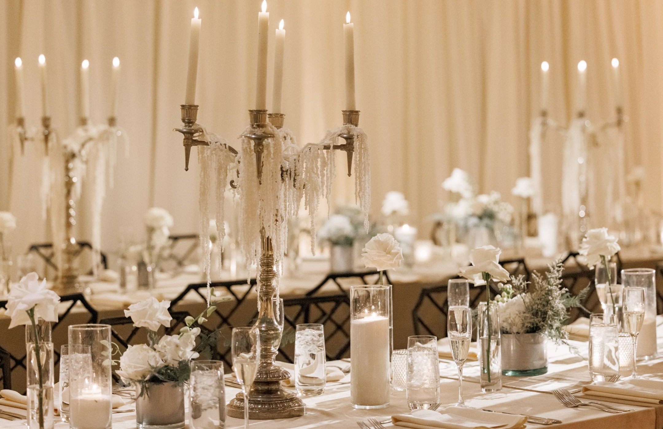 Reception tables dressed with white florals, candlelight, crystal candelabras, and elegant place settings for a timeless winter wedding reception at Winterthur.