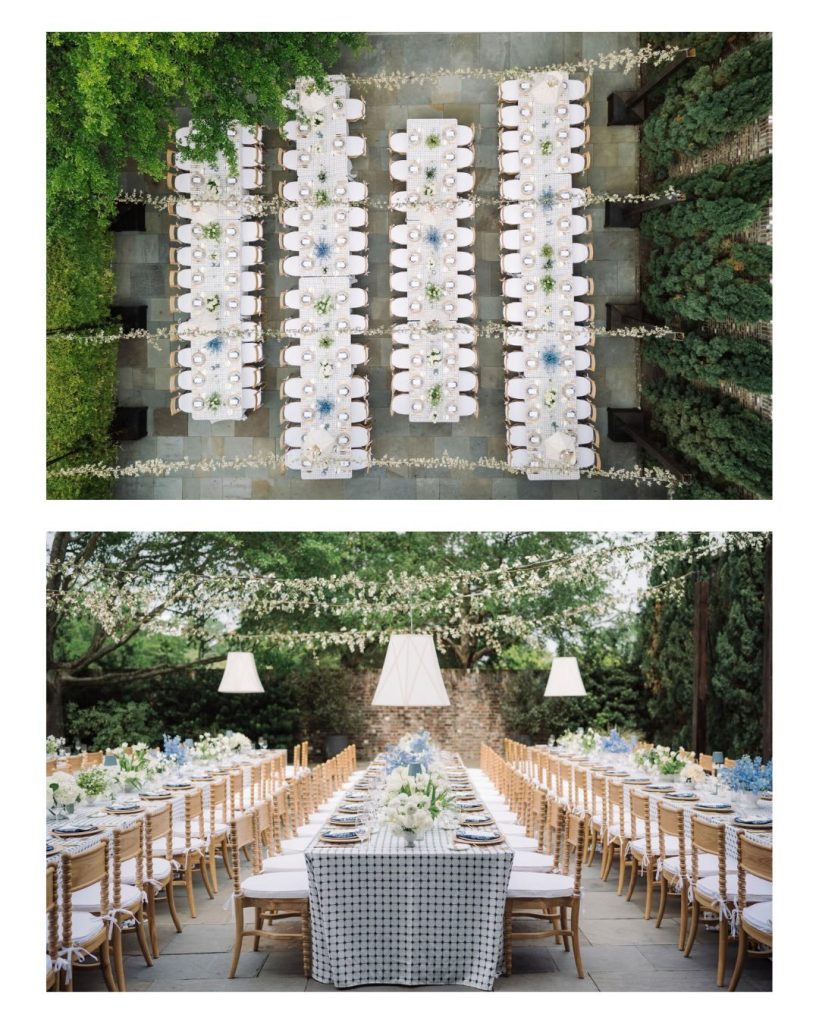 Aerial view of long reception tables arranged in rows between hedges, set with white linens and blue floral centerpieces.