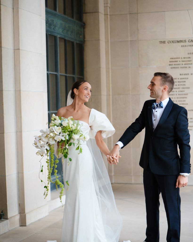 Bride and groom holding hands and laughing under the columns at Columbus Museum of Art
