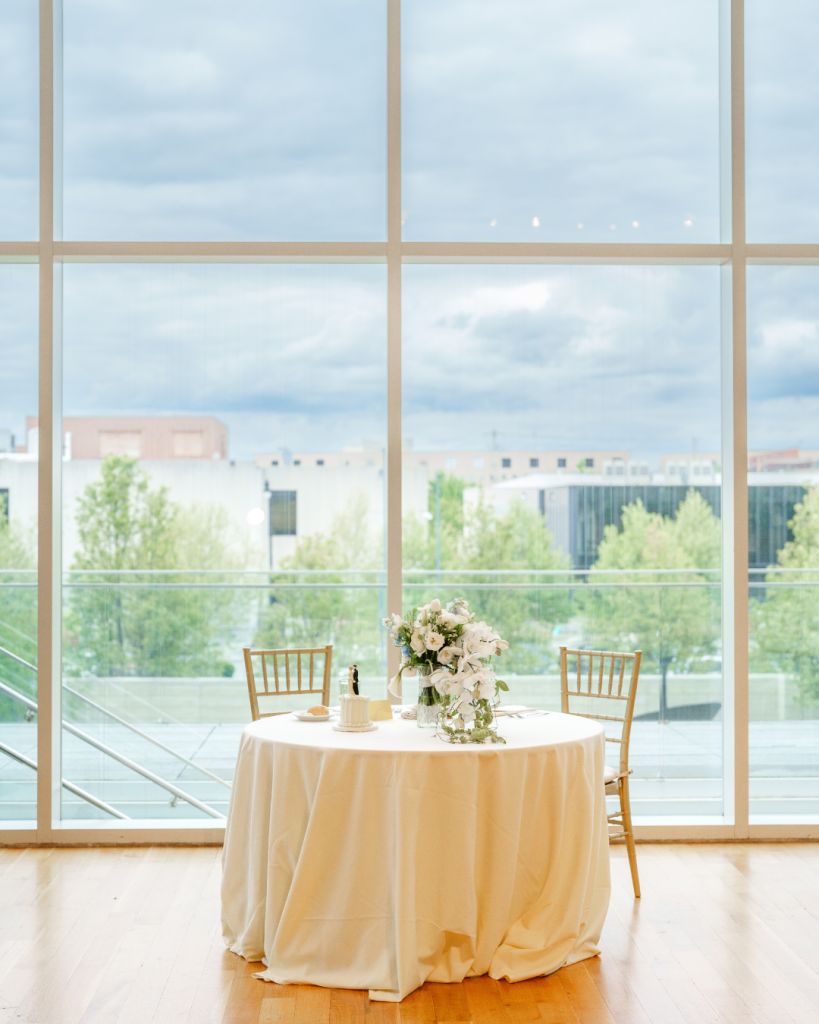 Sweetheart table with floral centerpiece and cake overlooking Columbus skyline through floor-to-ceiling windows