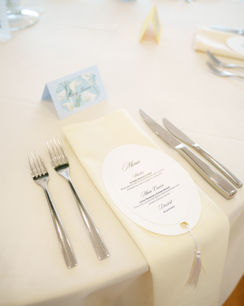 Wedding reception place setting with oval menu card, ivory linens, and calla lily place card