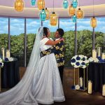 Hand-painted wedding portrait of a couple embracing beneath colorful pendant lights with blue and white floral arrangements.