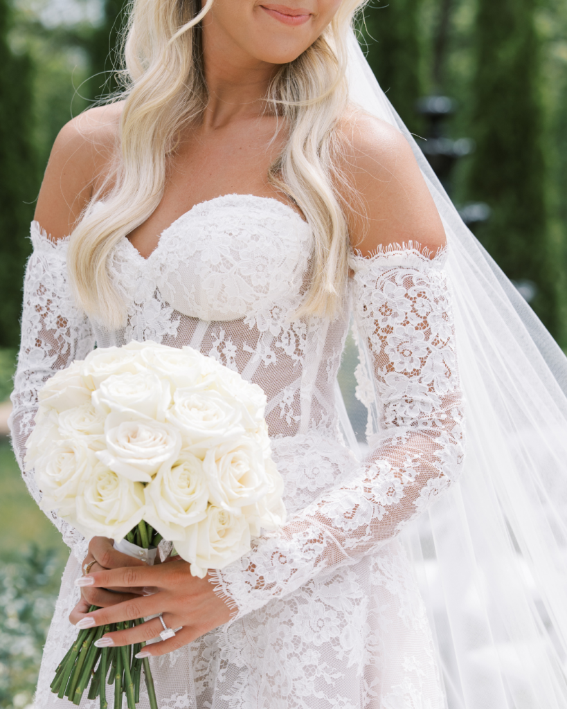 Close-up of Sierra’s long-sleeved lace Galia Lahav wedding gown, white rose bouquet, veil, and diamond ring.