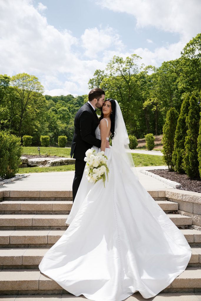 Groom embracing bride carrying a white and green bridal bouquet by Floral Play.