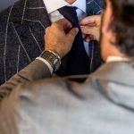 Professional clothier adjusting a navy tie on a client wearing a custom windowpane suit.