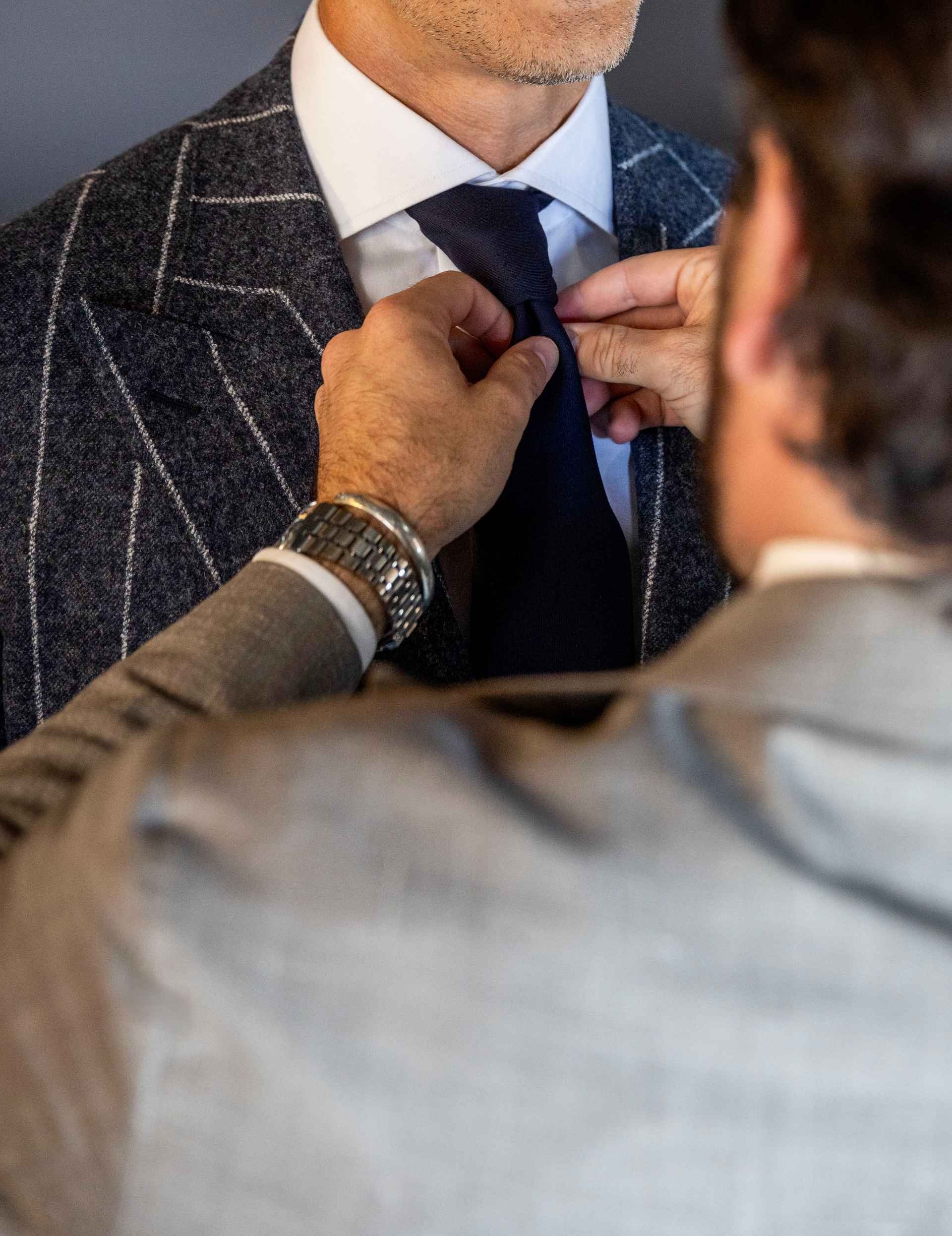 Professional clothier adjusting a navy tie on a client wearing a custom windowpane suit.