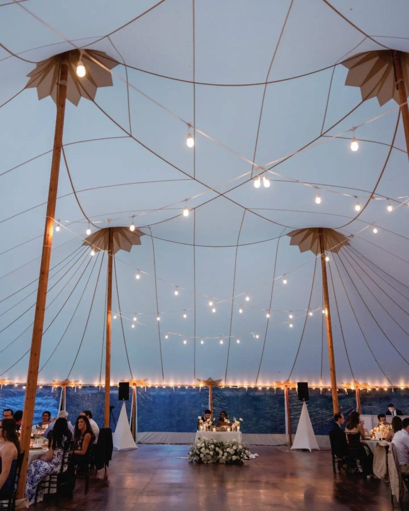 outdoor high ceiling tent with string lights and dance floor with sweetheart table in the middle