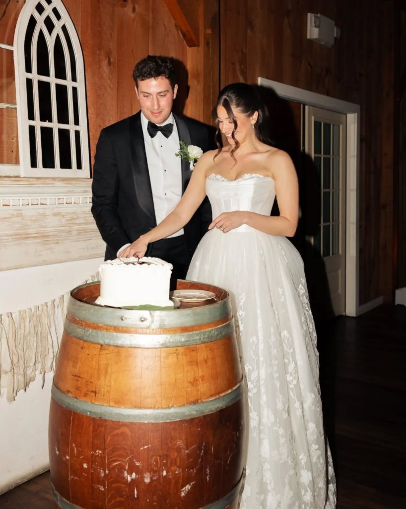 bride and groom cutting wedding cake on top of barrel during wedding reception in northern virginia