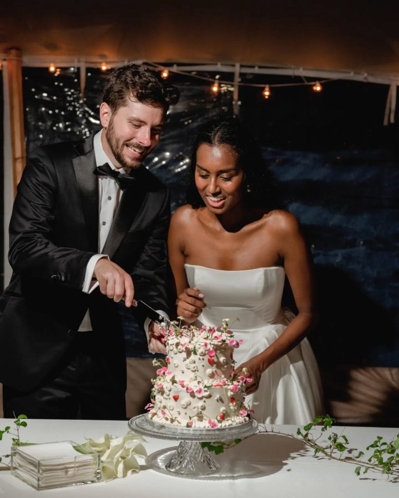 bride and groom cutting homemade wedding cake at wedding reception in sail tent at luxury outdoor wedding venue