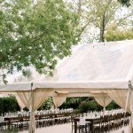 Clear tent wedding reception layout with long wooden tables, neutral drapery, and outdoor lighting ideas.