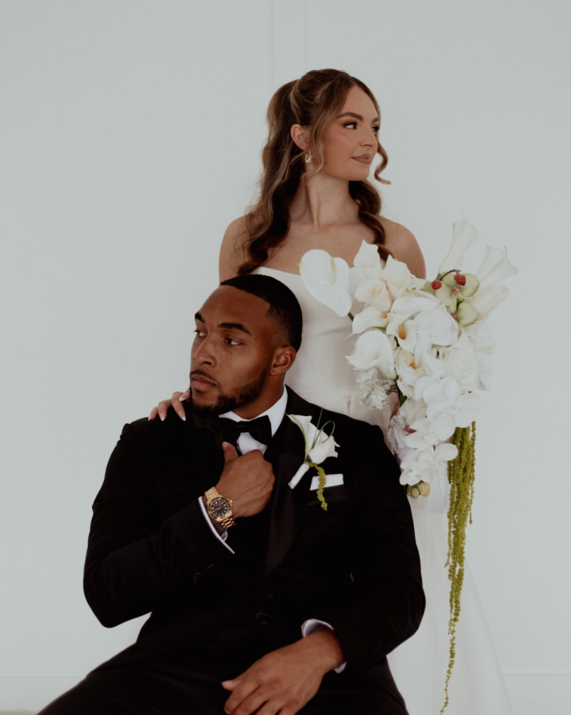 TreVeyon and Kenzie pose in formal wedding attire, with Kenzie holding a cascading white floral bouquet.
