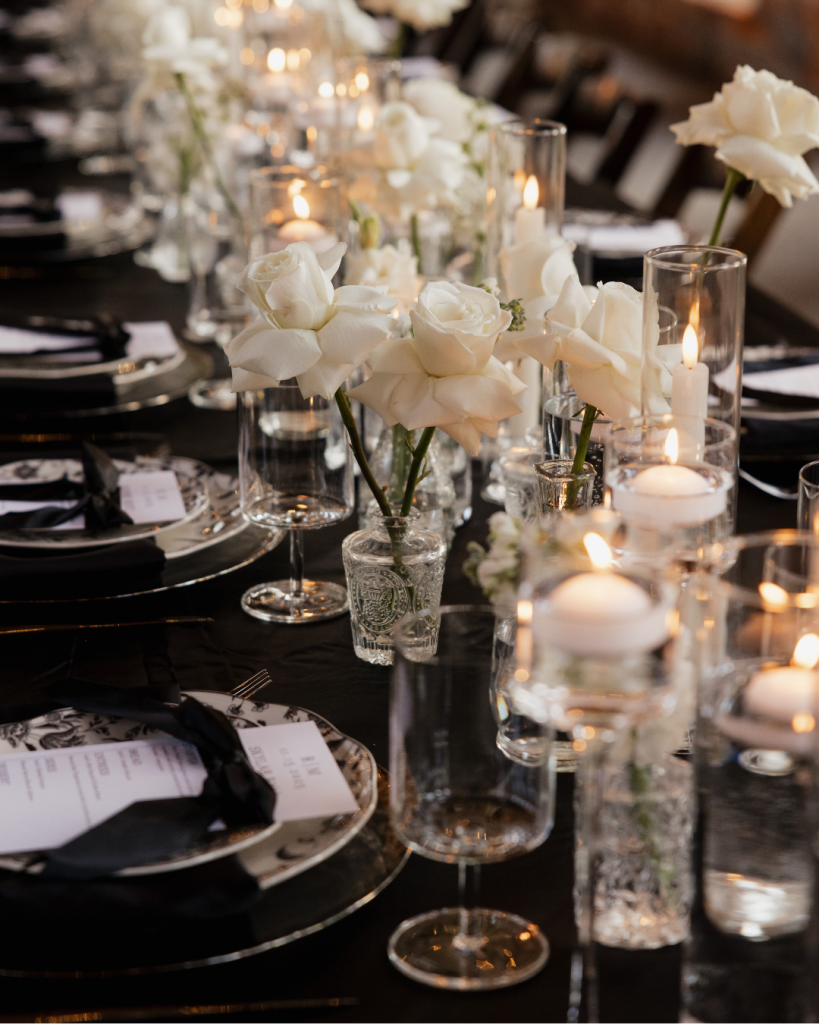 Elegant reception tables featuring white roses, candlelight, glass vessels, and black linens at The Providence Cotton Mill.