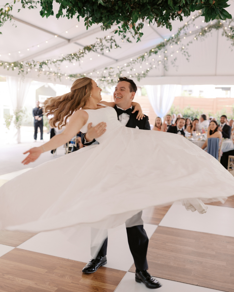 Bride and groom enjoy their choreographed first dance beneath greenery installations and café lights inside the reception tent at Van Landingham Estate.