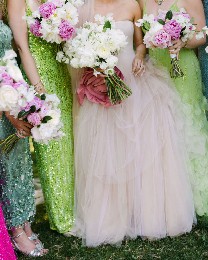 Bride in a blush wedding gown surrounded by bridesmaids in colorful gowns holding pink and white summer bouquets.