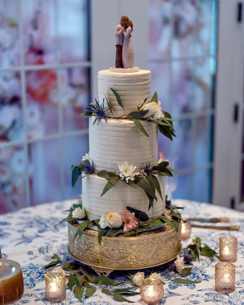 Three tier white wedding cake decorated with fresh flowers and greenery displayed at the reception.