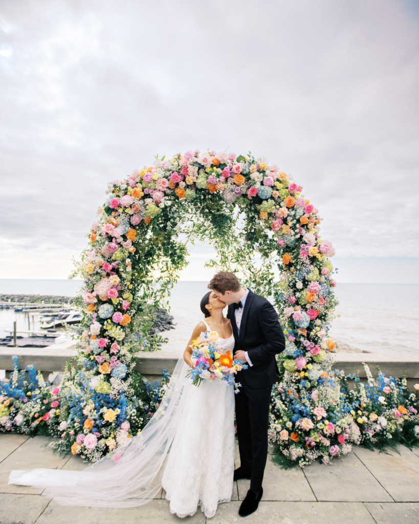 Bright floral arch with bride and groom kissing under it at Shoreby Club in Cleveland