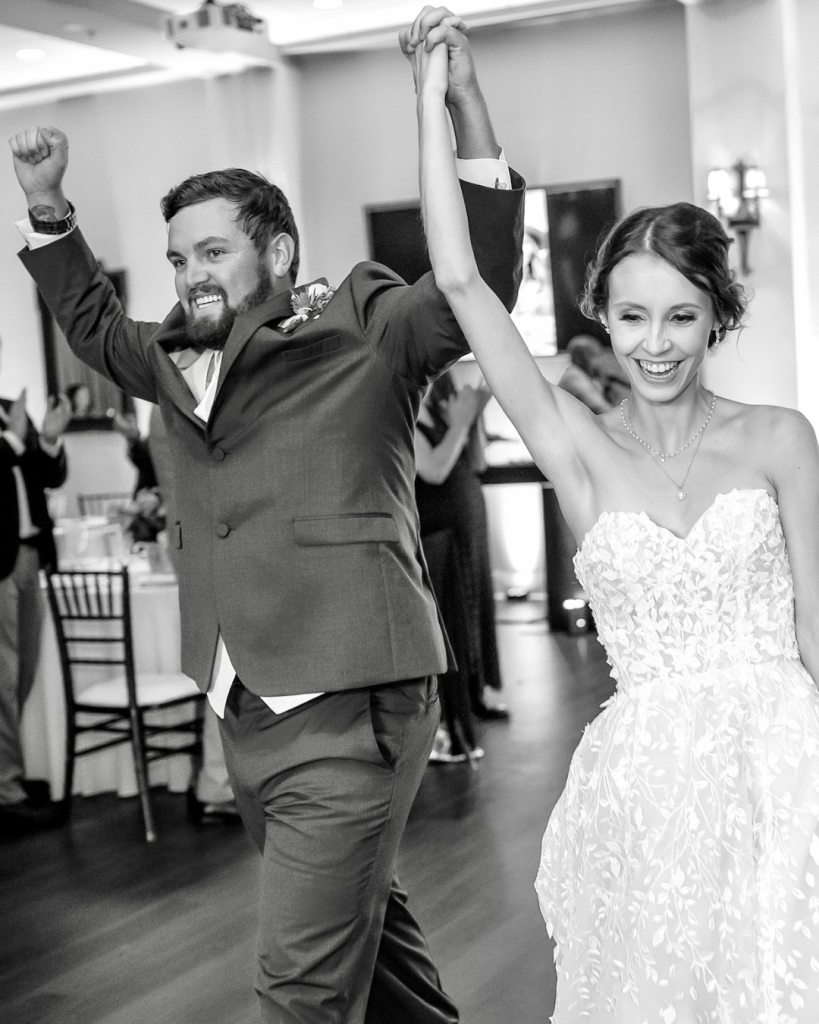 Bride and groom celebrating on the dance floor after being announced at their reception with joyful expressions.