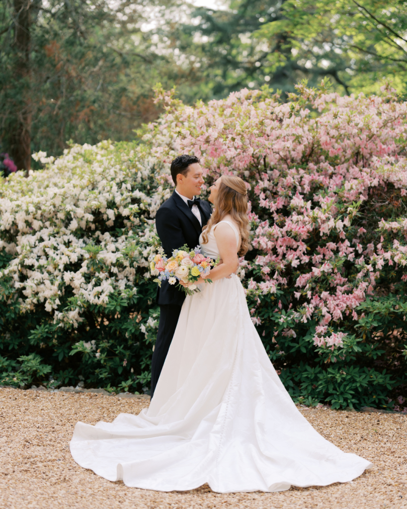 Bride and groom embrace in front of blooming pink and white azaleas during spring wedding portraits at Van Landingham Estate in Charlotte.