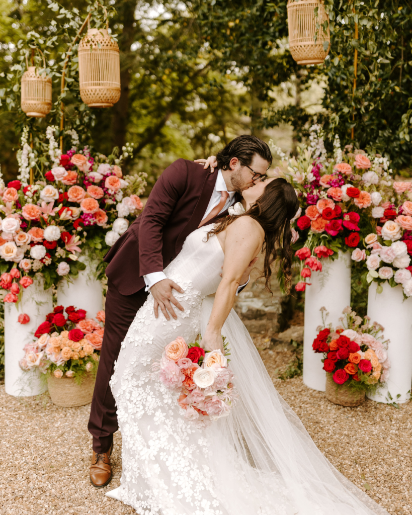 Bride and groom share a kiss beneath a vibrant floral ceremony installation with woven lanterns and lush greenery at Van Landingham Estate in Charlotte.