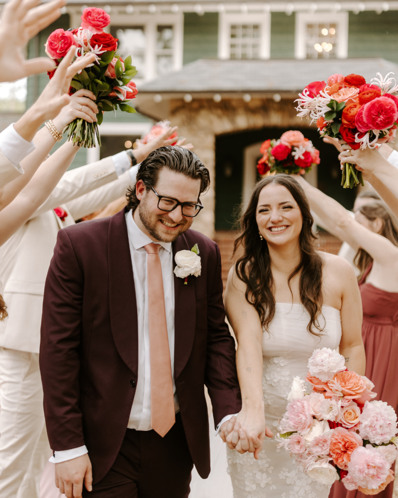 Newlyweds walk through a bouquet tunnel while smiling after their ceremony at Van Landingham Estate in Charlotte, North Carolina.