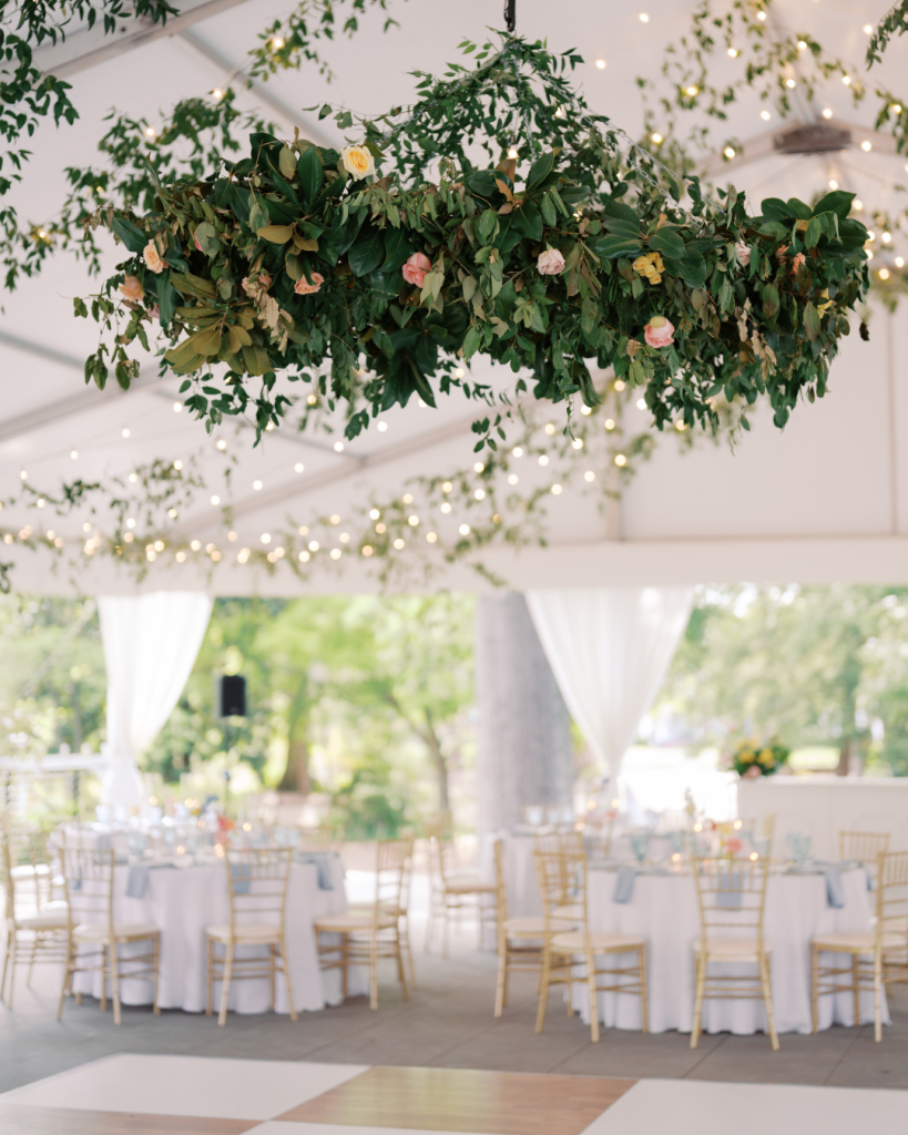 Reception tent featuring suspended greenery installation, café lighting, gold chairs, and elegant spring décor at Van Landingham Estate in Charlotte.