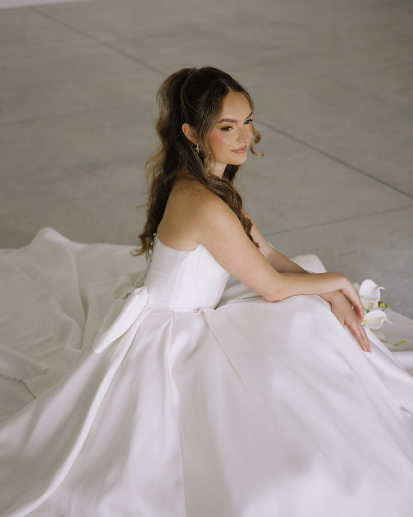 Kenzie sits in her strapless white wedding gown, surrounded by the flowing train of her dress.