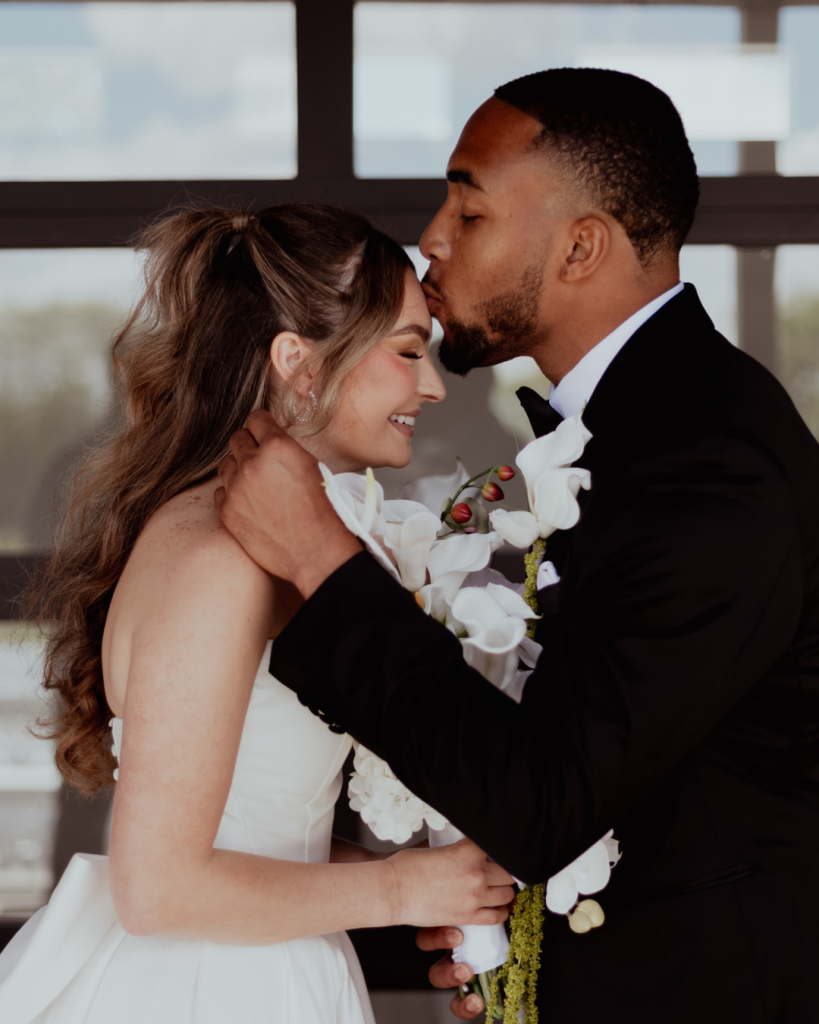 TreVeyon kisses Kenzie’s forehead while she holds her cascading white floral bouquet.