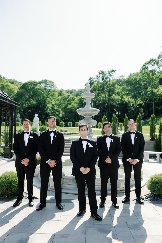 Groom and groomsmen standing in front of European-inspired fountain at Knotting Hills Wedding Venue & Resort.