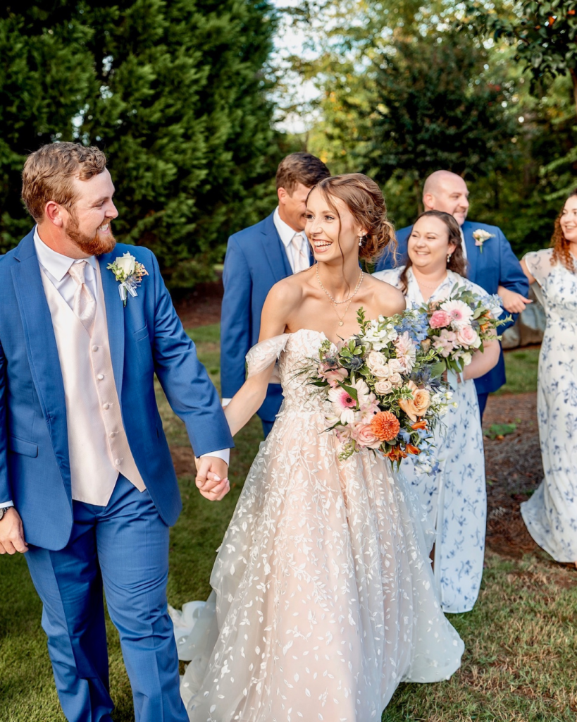 Bride and groom walking with their wedding party after the ceremony, smiling and carrying colorful bouquets at The Riverwalk Event Venue.