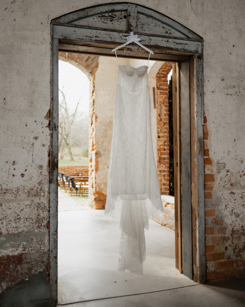 Lace wedding gown hanging in the historic brick doorway at The Providence Cotton Mill wedding venue.
