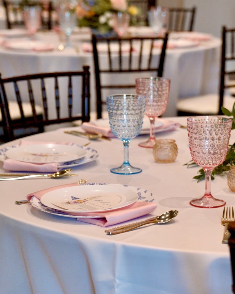 Reception table featuring blue and white patterned dinnerware, pastel goblets, blush napkins, and elegant place settings.
