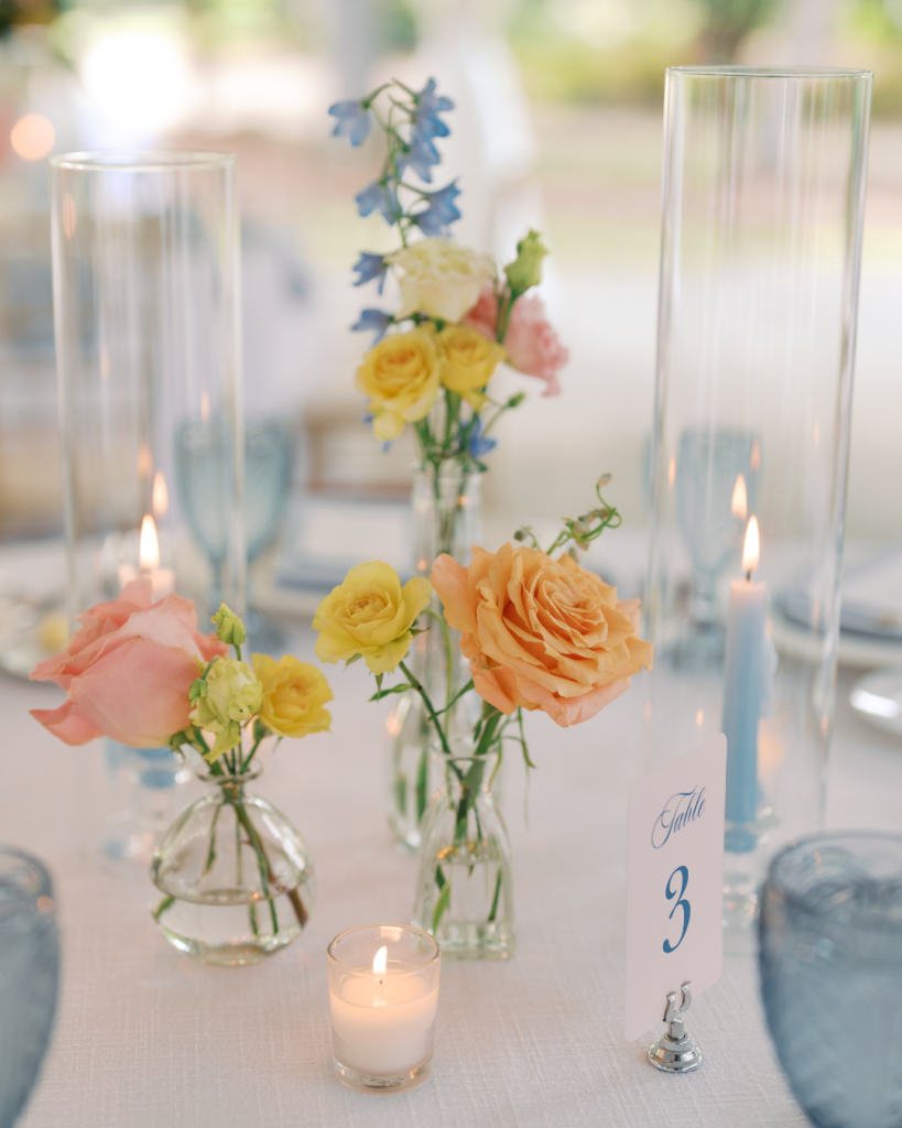 Spring wedding centerpiece featuring pastel roses, blue delphinium, candles, and elegant glass vessels at a Charlotte wedding reception.