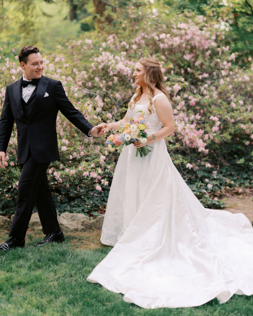 Bride and groom walk hand in hand through blooming azaleas following their ceremony at Van Landingham Estate in Charlotte.