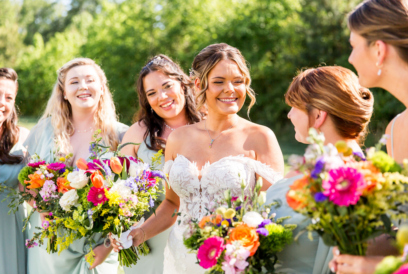 Bride smiling with her bridesmaids while holding colorful bouquets during a Boutique Bride wedding in Delaware.
