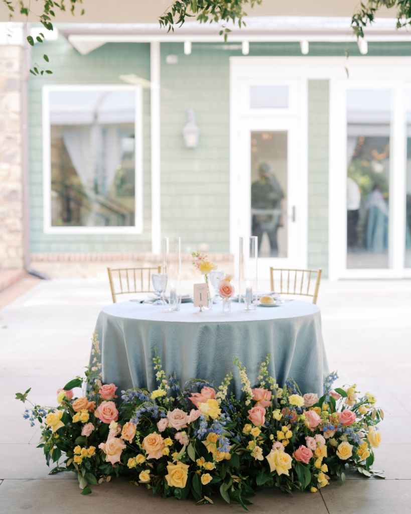 Sweetheart table featuring lush floral meadow installation and soft blue linens at an elegant Charlotte wedding reception.
