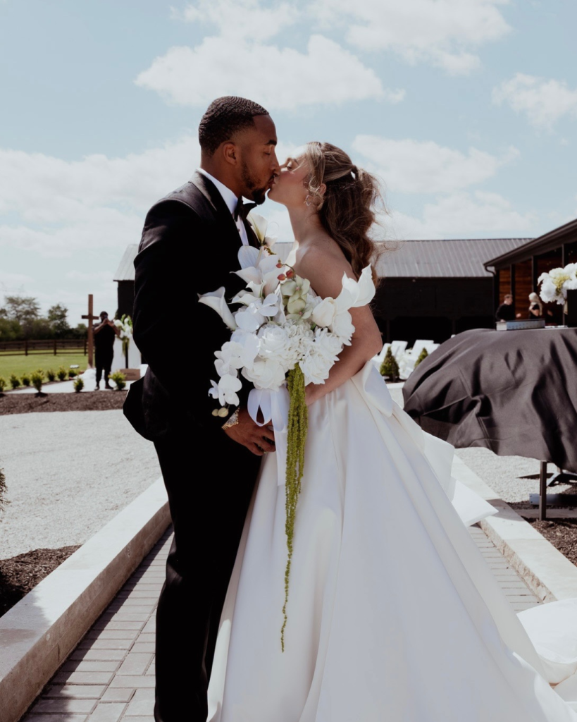 TreVeyon and Kenzie kiss outdoors at Twin Run Farm, with Kenzie’s white bouquet and the venue’s black exterior behind them.
