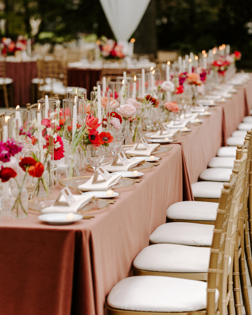 Elegant reception tables lined with candles and vibrant spring floral arrangements beneath a draped tent at Van Landingham Estate.