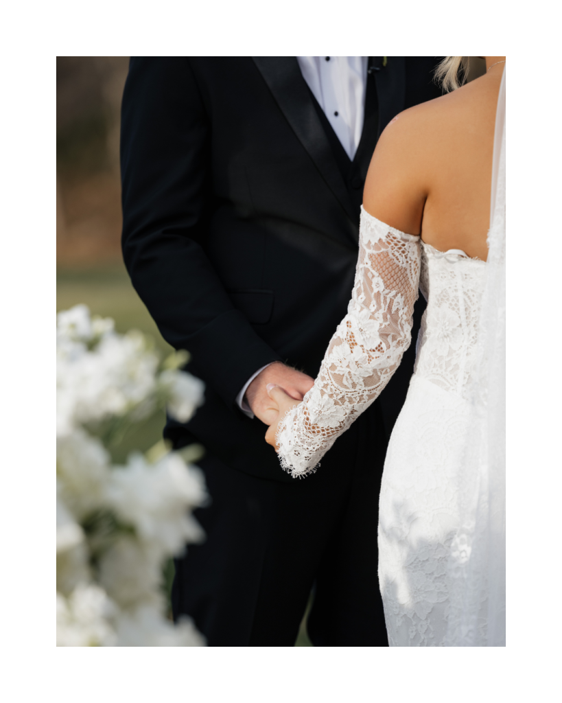 Close up of bride and groom holding hands highlighting lace sleeve details and classic bridal styling.