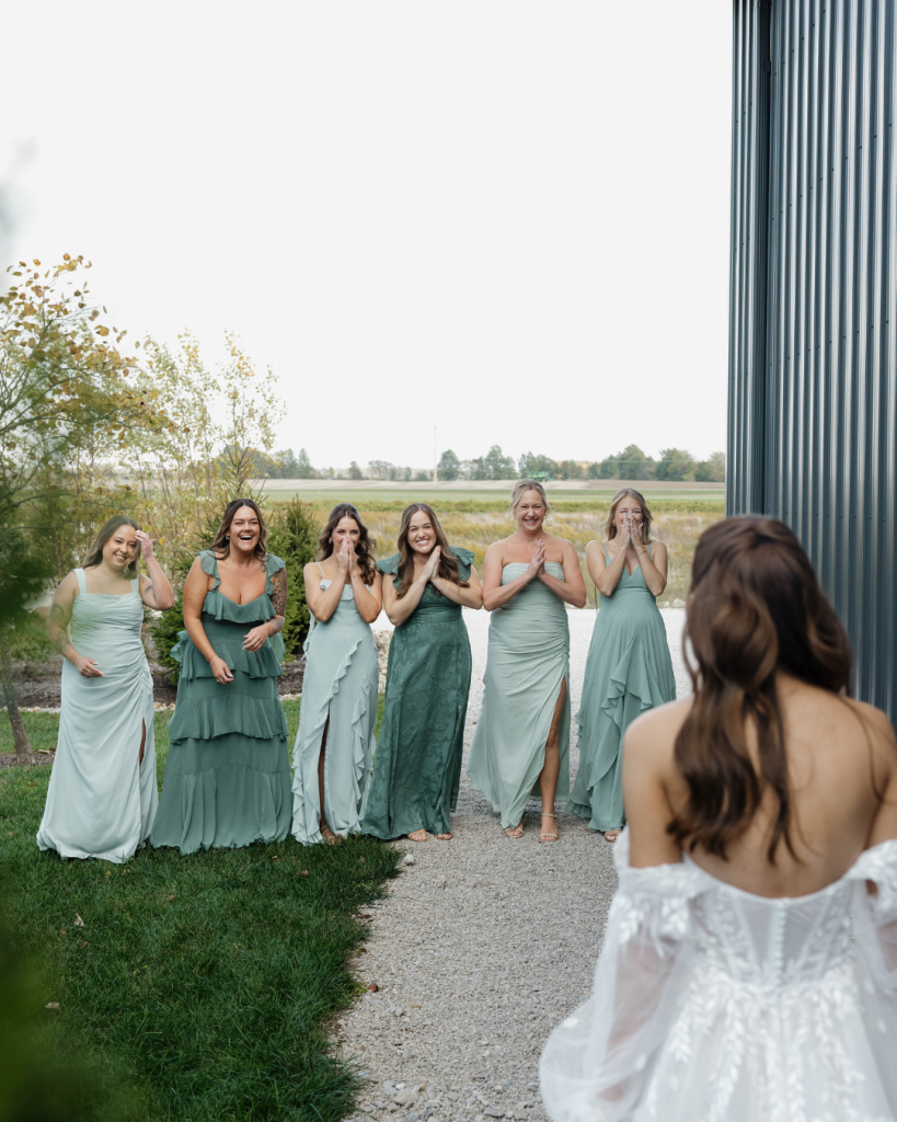 Bridesmaids in varying sage green dresses hold bouquets of white flowers, peach carnations and greenery.