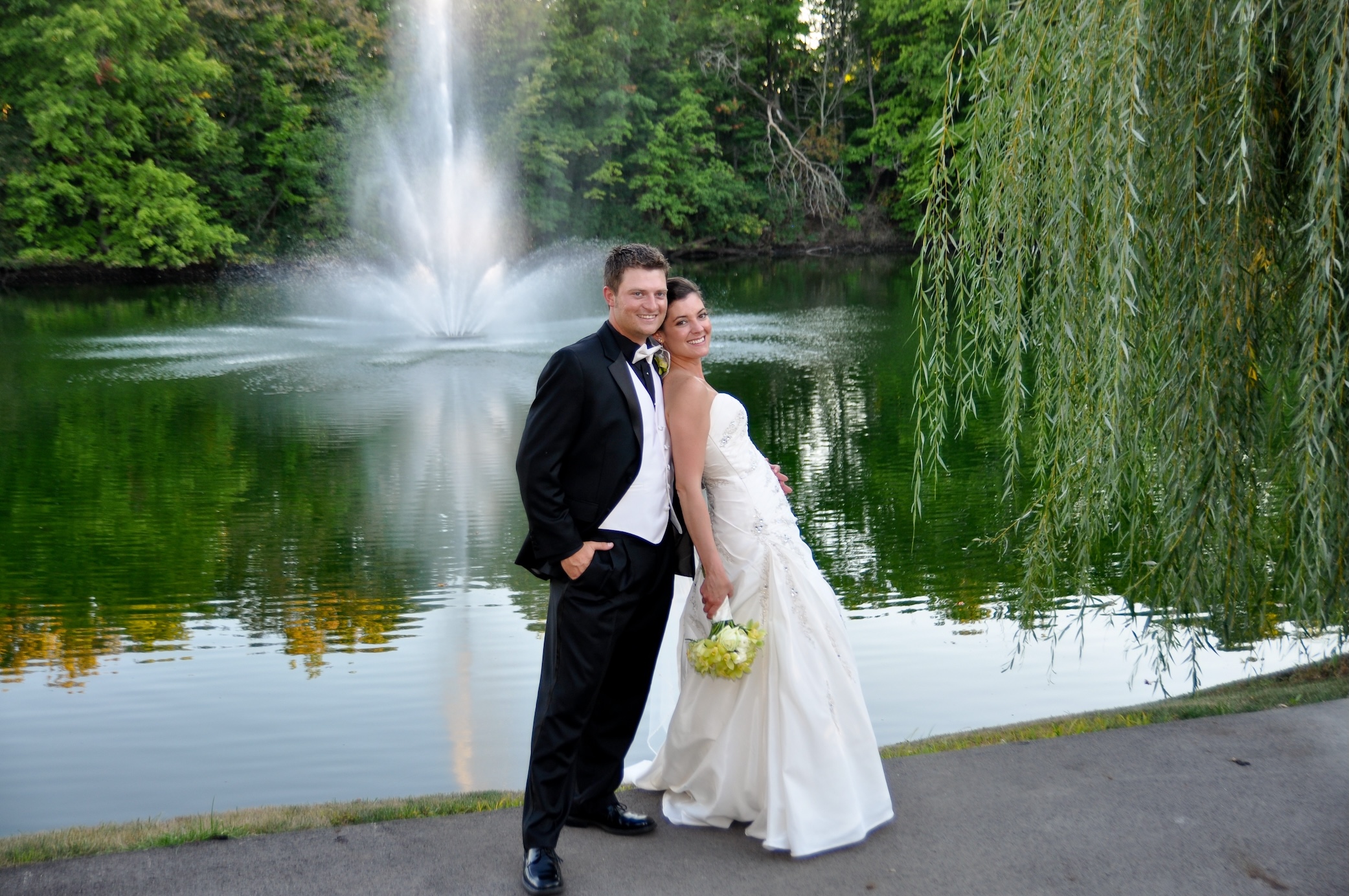 Newlywed couple posing beside a tree-lined pond and fountain at Brookside Golf & Country Club in Columbus, Ohio.