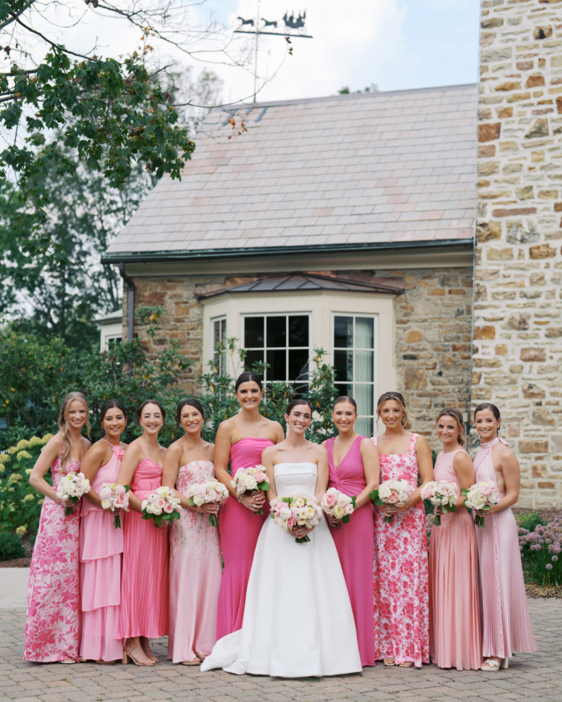 Caroline poses with her bridesmaids in a mix of solid pink and floral dresses outside a stone building in Columbus.