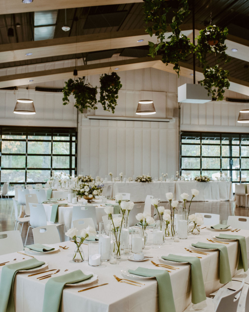 Modern Retreat 21 reception with white linens, sage green napkins, gold flatware, white roses and suspended greenery.