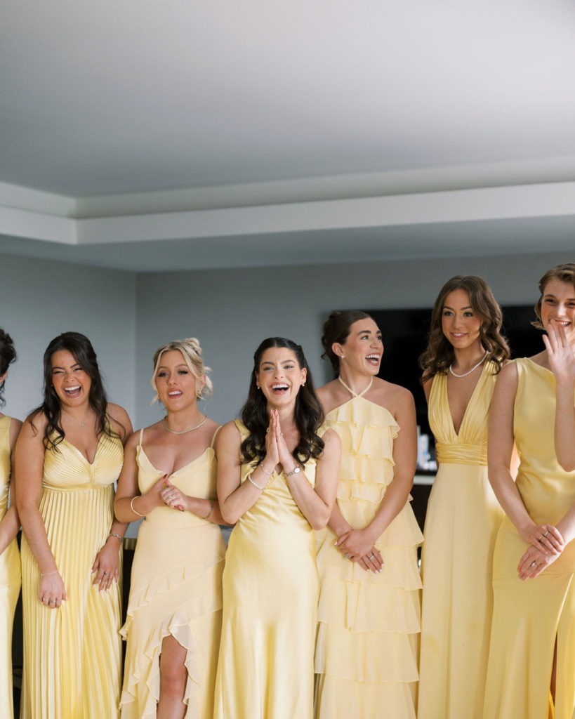 Bridesmaids in mismatched yellow dresses smile and react during the wedding morning.