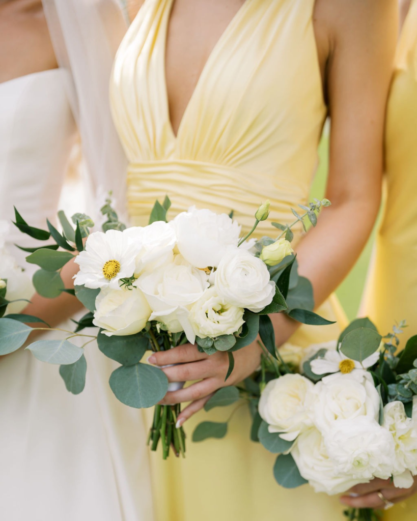 Bridesmaid in a soft yellow dress holds a bouquet of white flowers and eucalyptus greenery.