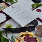 Wedding invitation suite with burgundy accents and wax seals styled among flowers.